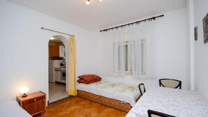 A small, well-lit room with a bed, a table, and a chair. There is a door leading to a kitchen area. - Apartments Lucia (Senj)