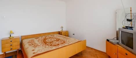 A bedroom with a wooden bed, a nightstand, a dresser, a television, and a chandelier.