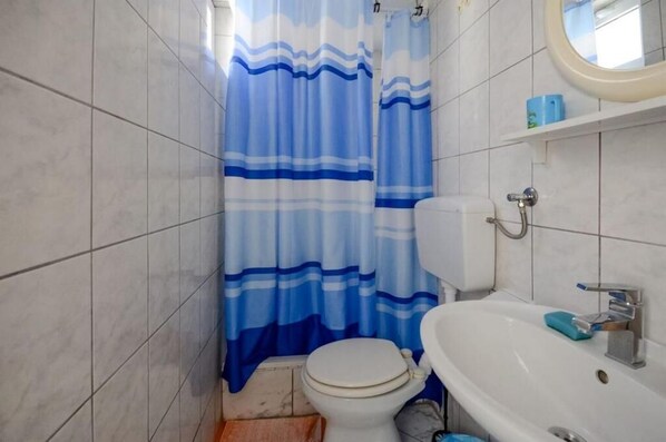A bathroom with a toilet, sink, and shower curtain. - Apartments Lucia (Senj)