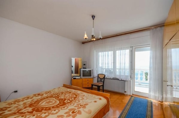 A bedroom with a bed, a television, a chair, and a window with curtains. - Apartments Lucia (Senj)