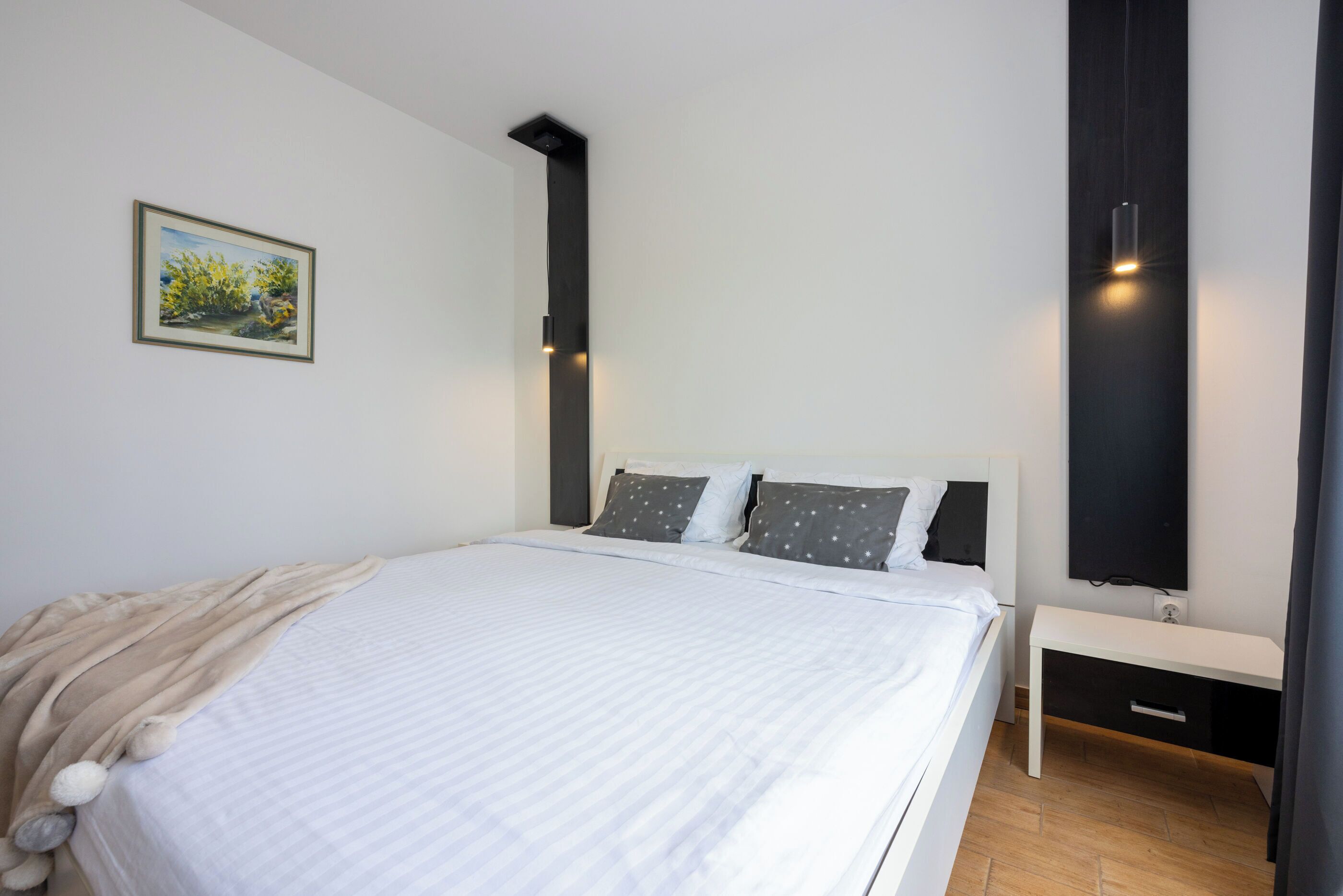 Une chambre à coucher moderne avec un grand lit, une table de chevet, un téléviseur fixé au mur et un tableau accroché au mur.