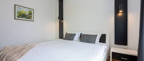 Une chambre à coucher moderne avec un grand lit, une table de chevet, un téléviseur fixé au mur et un tableau accroché au mur.