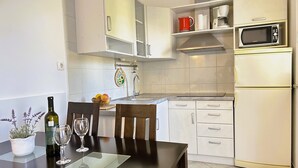 A modern kitchen with white cabinets, a microwave, and a sink. There is a dining table with chairs and a wine bottle.