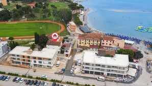 Eine Küstenstadt mit Strand, Sportplatz und mehreren Gebäuden, darunter ein Hotel mit rotem Dach.