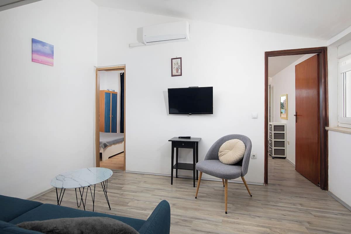 A modern living room with a sofa, a small table, a chair, a TV, and a wardrobe.