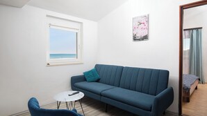 Ein Zimmer mit blauem Sofa, einem kleinen runden Tisch und Meerblick durch ein Fenster.
