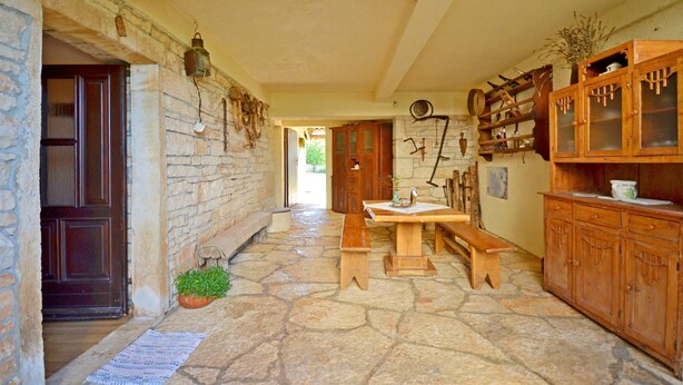 A stone-floored corridor with wooden benches, a wooden door, and a cabinet with glass doors. - Apartment Srblin (Zminj)