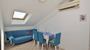 Una habitación pequeña y acogedora con tragaluz, un sofá, una mesa de comedor con sillas y un equipo de aire acondicionado.