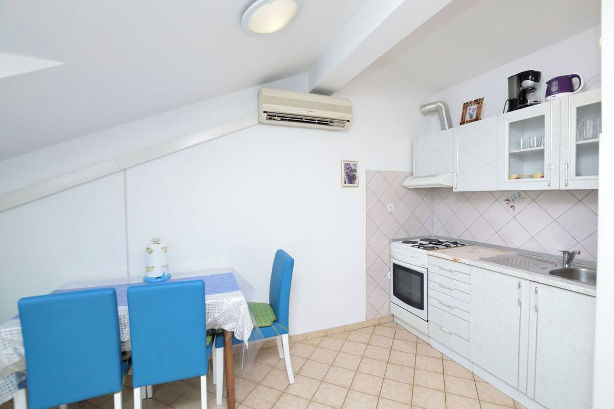 A compact kitchen with a dining area, white cabinets, a stove, and a ceiling-mounted air conditioner.