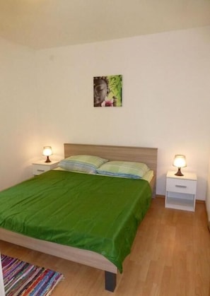 Un lit simple avec une couvre-lit verte, deux tables de chevet avec des lampes et un tableau accroché au mur.