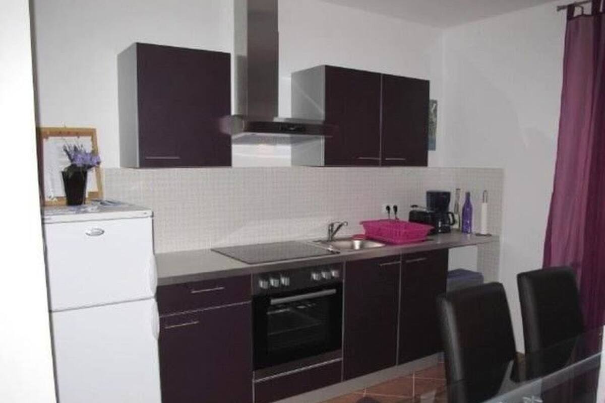 A compact kitchen with a refrigerator, oven, sink, and a dining area with chairs.