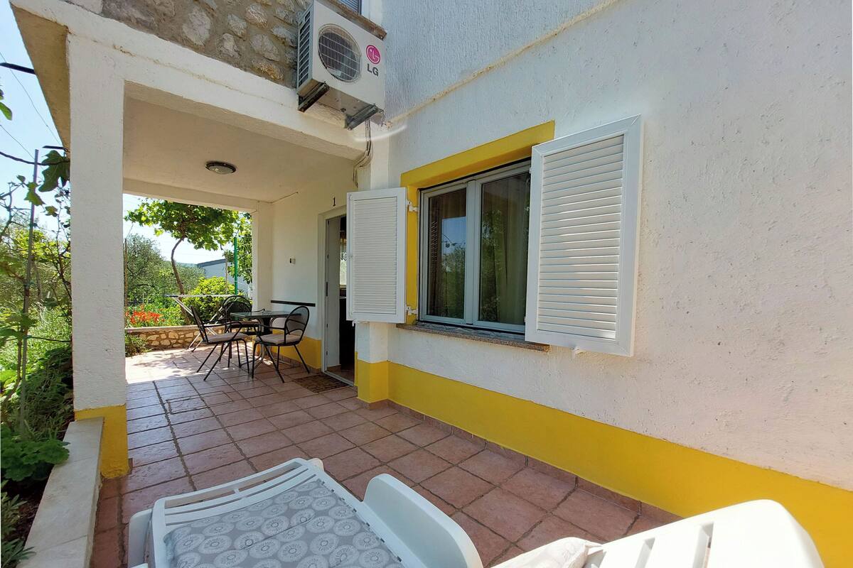 A covered patio area with a table and chairs, a window with shutters, and an air conditioning unit.