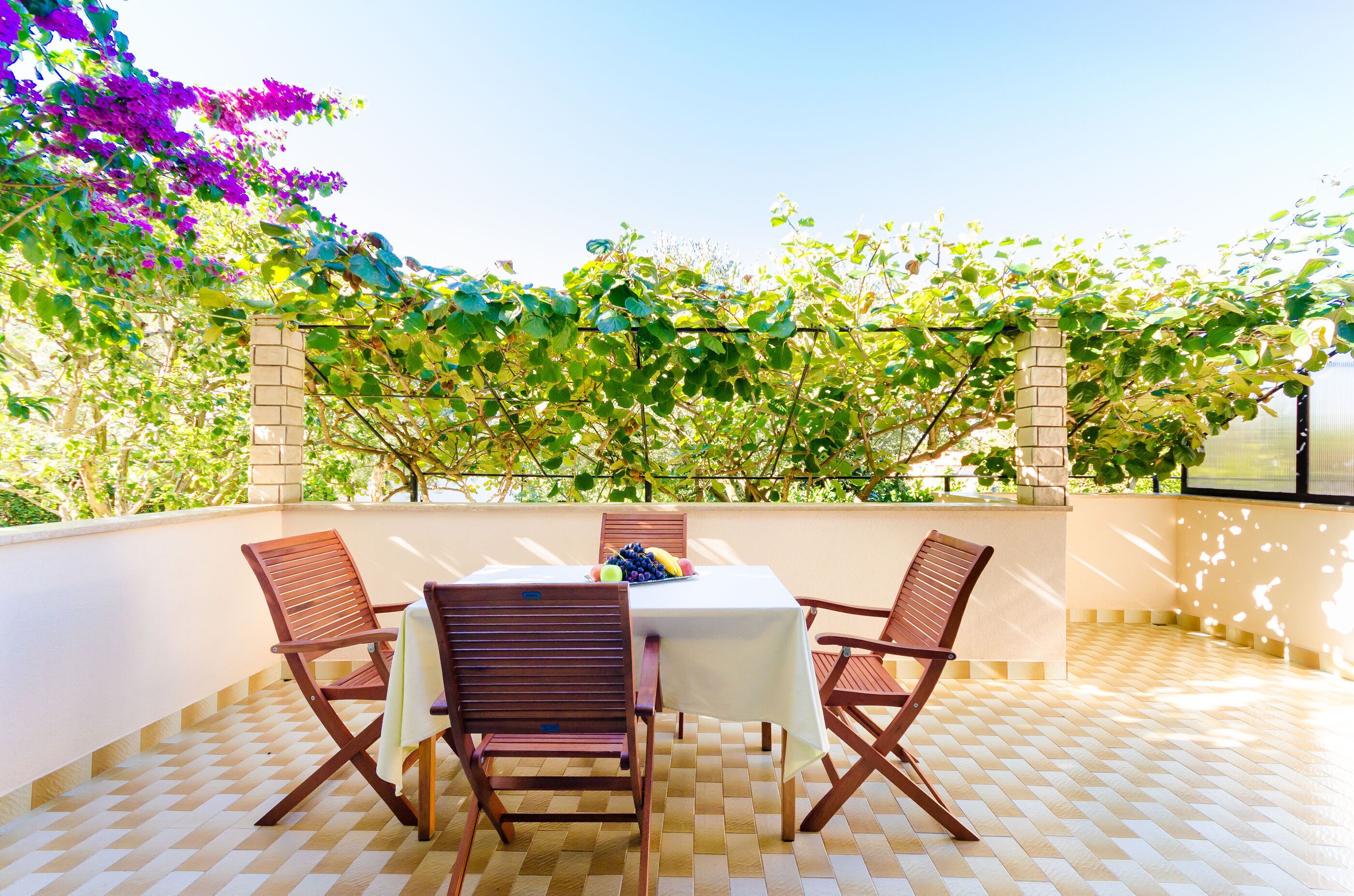 Un patio con una mesa y sillas, rodeado de un muro de ladrillo y vegetación.