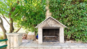 Camino esterno in pietra con griglia metallica, circondato da pareti in pietra e vegetazione.