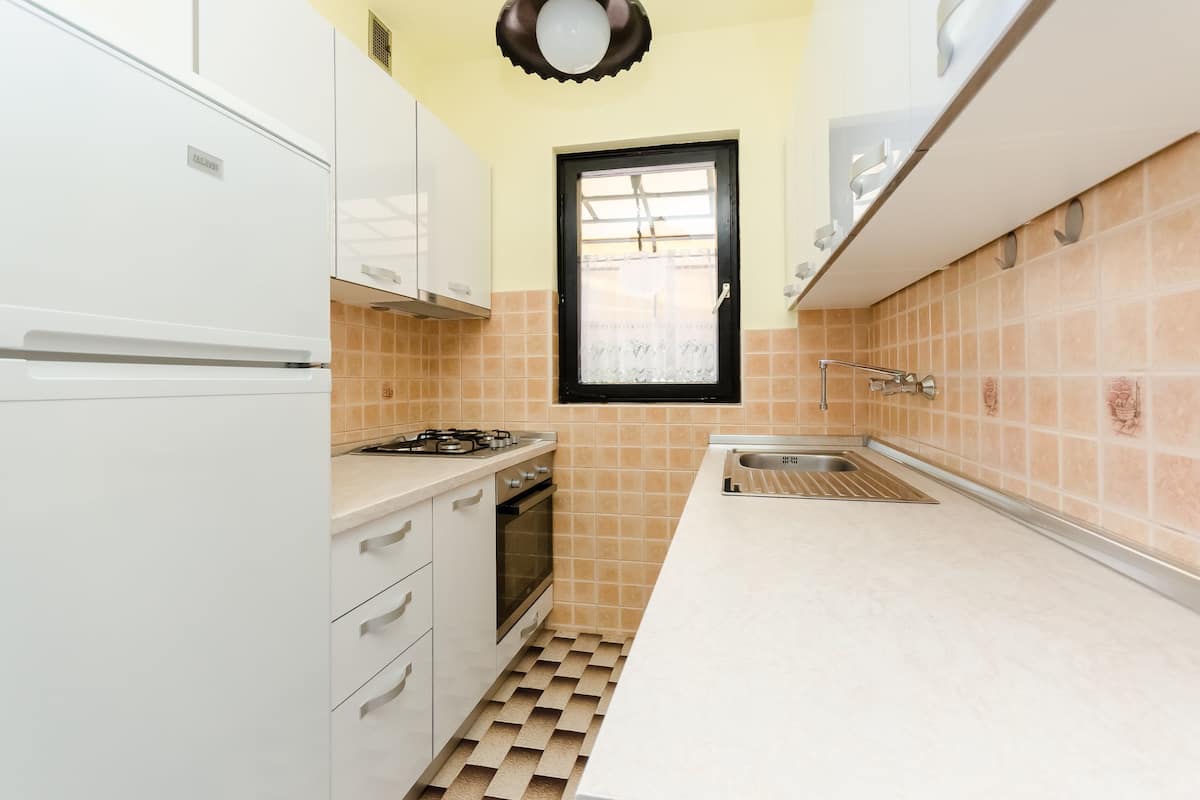 A compact kitchen with white cabinets, a gas stove, an oven, and a window with a black frame.