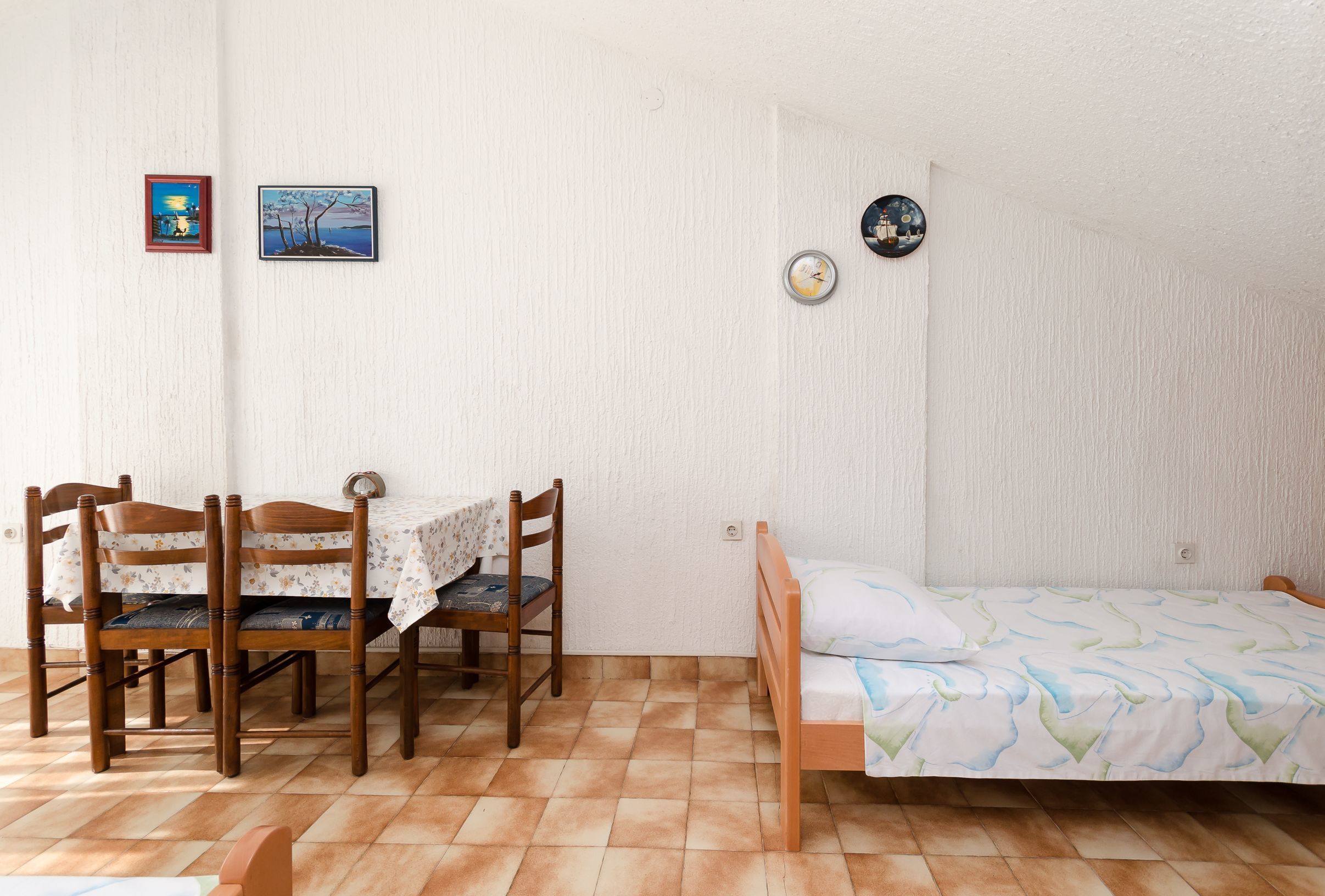 A room with a bed, a table with chairs, and two wall-mounted clocks.