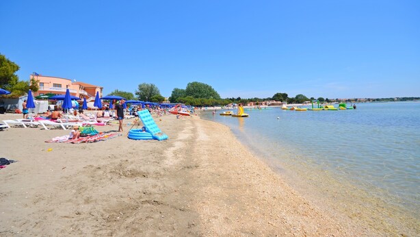 Una spiaggia con acqua cristallina, ombrelloni e lettini.