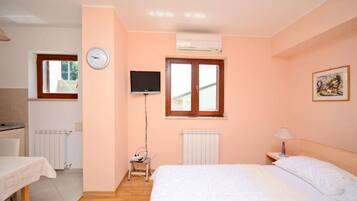 Une chambre à coucher avec un lit, une télévision, une fenêtre, un radiateur et une table avec une chaise.