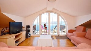 A spacious living room with a large arched window, a flat-screen TV, a sofa, and a small table with a vase of flowers. - Apartments Ivanka (Senj)