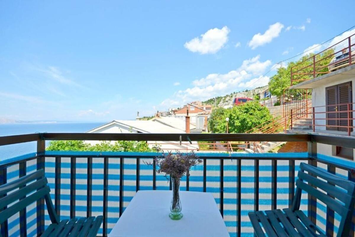 A balcony with a table and chairs, a vase with flowers, and a view of the sea and buildings.