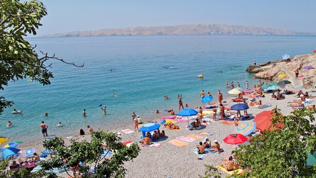 A beach with people swimming and sunbathing, surrounded by rocky cliffs and clear blue water. - Apartments Ivanka (Senj)