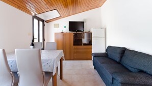 A compact living space with a dining table, chairs, a sofa, a television, and a refrigerator. - Apartments Ratko (Rakalj)