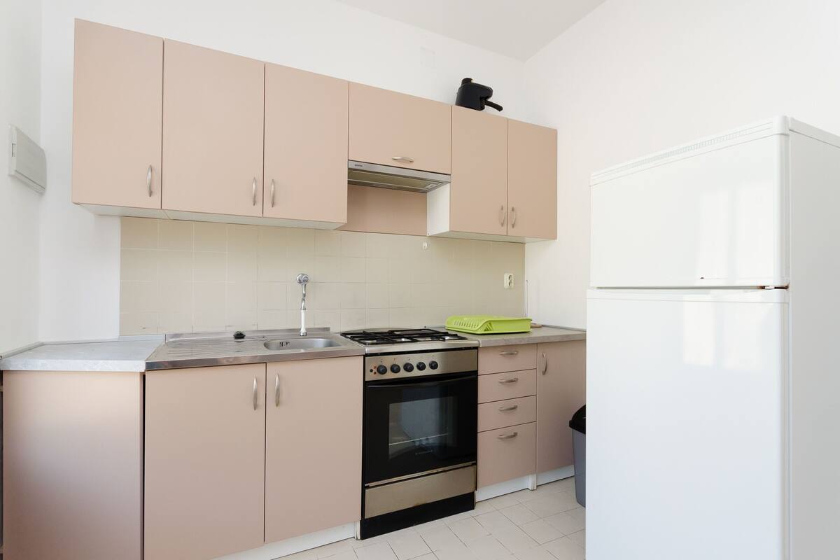 A kitchen with light pink cabinets, a stainless steel stove, a white refrigerator, and a green dish rack.