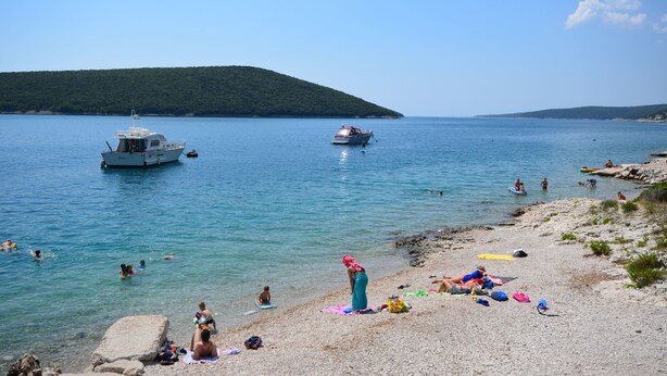 A beach with clear water, boats, and people swimming and sunbathing. - Apartments Ratko (Rakalj)