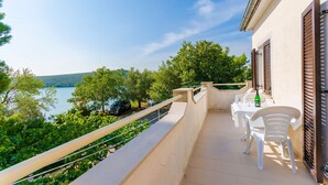 A balcony with outdoor seating, overlooking a lake and trees. - Apartments Ratko (Rakalj)
