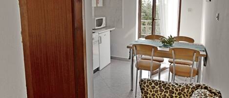 A hallway with a wooden door, a kitchenette, a dining area with a table and chairs, and a leopard-print sofa.