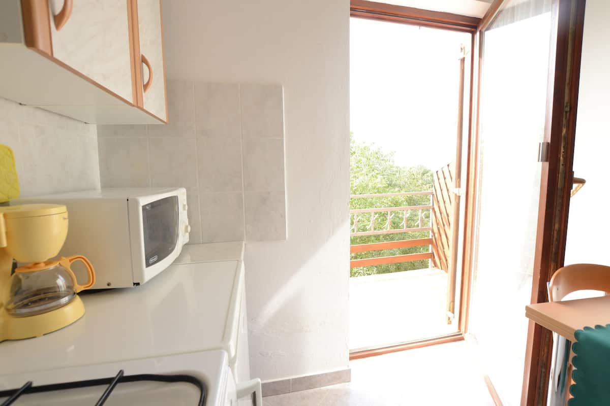 A kitchen with a microwave, coffee maker, and a view of a balcony with a wooden railing.