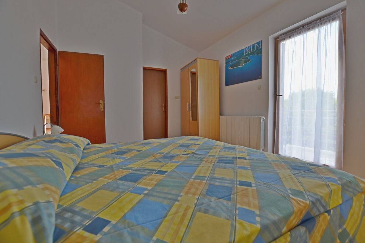 A bedroom with a bed, a wardrobe, a door, a radiator, and a window with curtains.