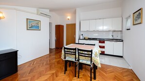 A compact kitchen with white cabinets and a wooden dining table with chairs. - Apartments Dragica (Stinjan)