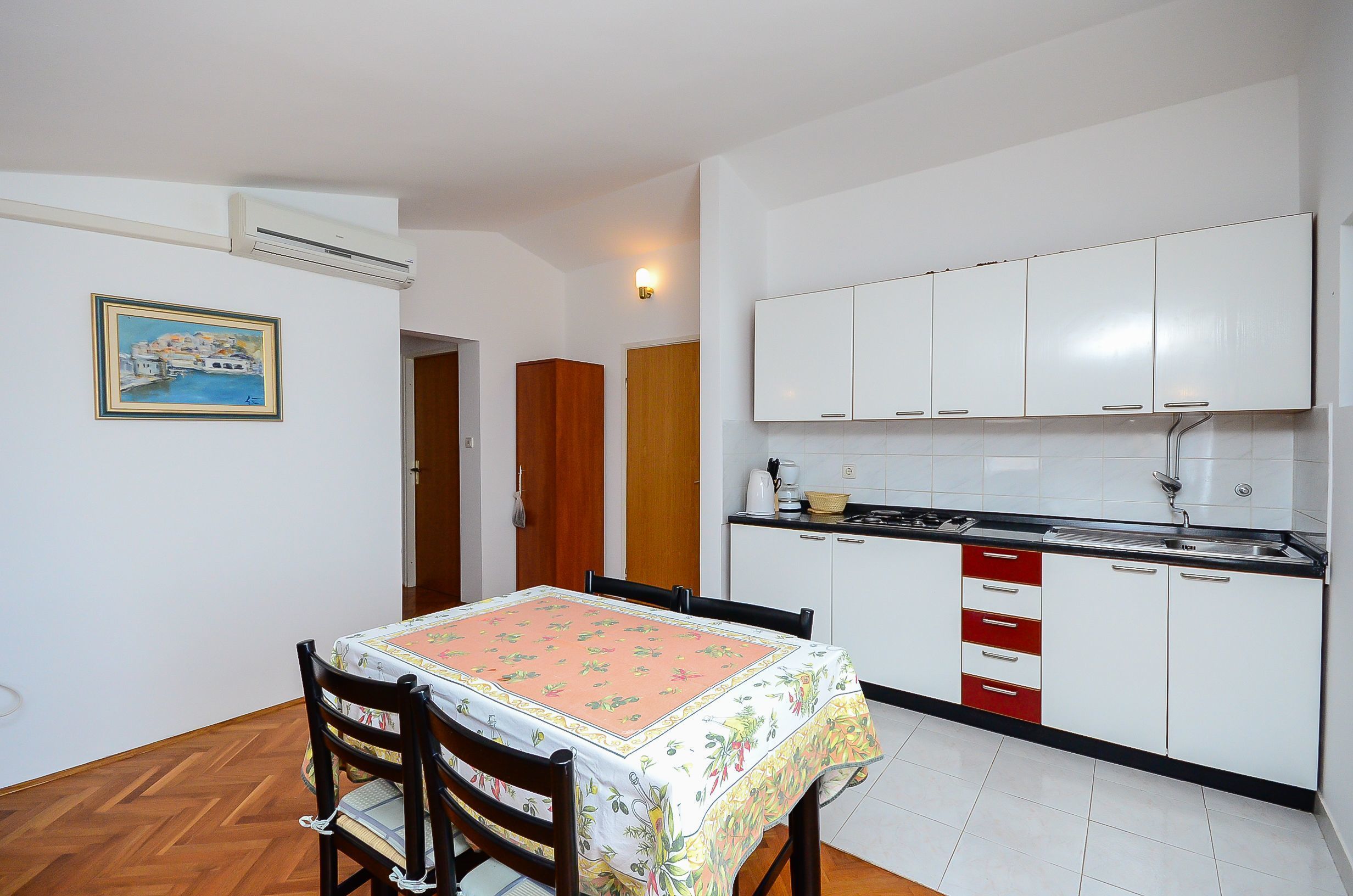A compact kitchen with white cabinets, a dining table with a floral tablecloth, and a wooden chair.