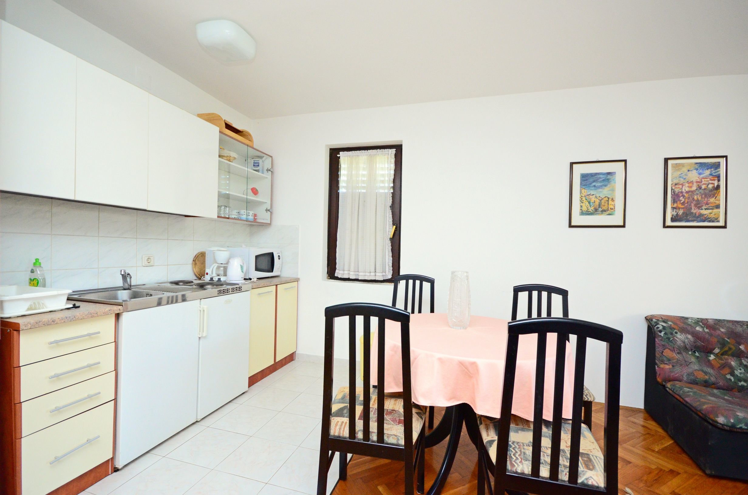 Cocina compacta con armarios blancos, microondas y pileta. Hay una mesa de comedor con sillas y un sofá en la zona de estar.