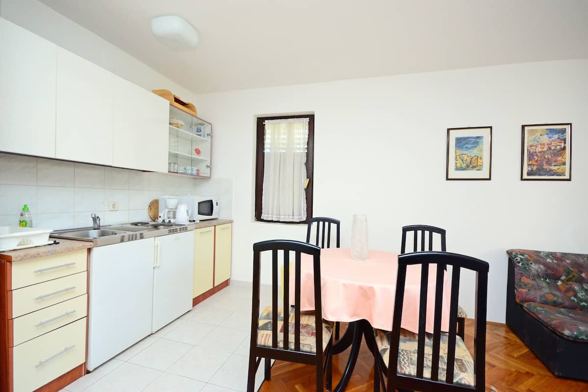 A compact kitchen with white cabinets, a microwave, and a sink. There is a dining table with chairs and a sofa in the living area.