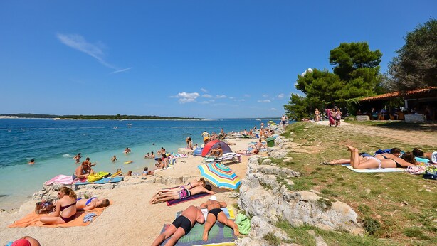 A beach with people sunbathing, swimming, and relaxing under umbrellas. - Apartments Dragica (Stinjan)