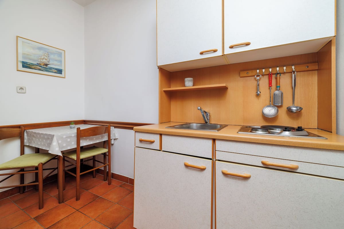 A compact kitchen with a dining area, featuring a small table and chairs, a sink, and a wooden countertop.