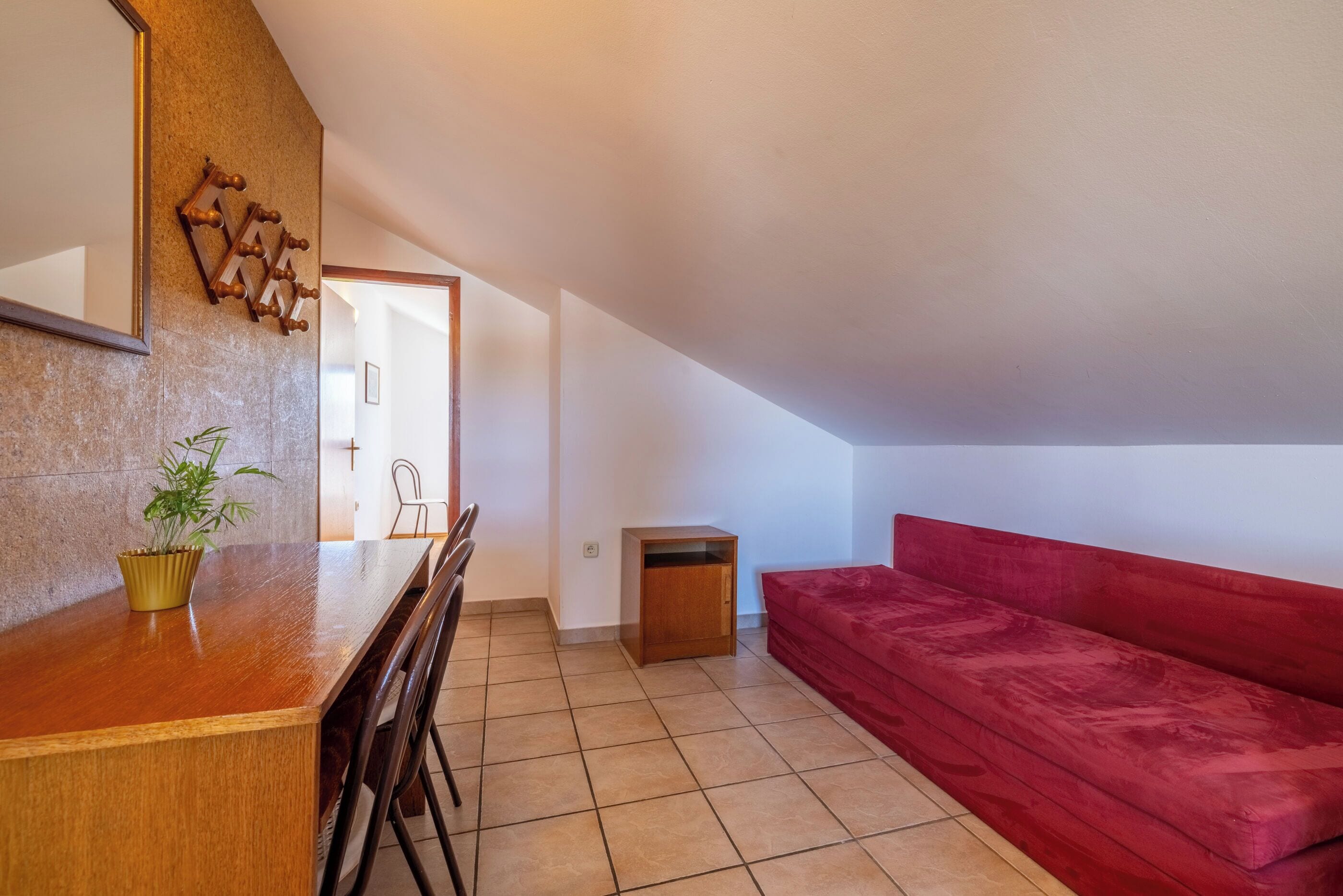 A small, modern living space with a wooden dining table, chairs, a red sofa, and a small cabinet.