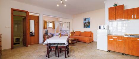 A spacious living area with a dining table, orange sofa, and kitchen area with wooden cabinets.