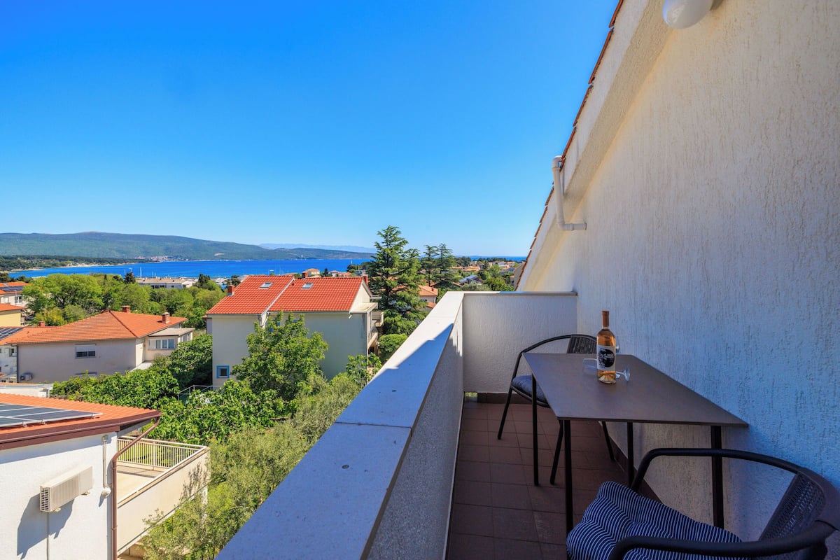 A balcony with a table and chairs, overlooking a scenic view of a lake and buildings.