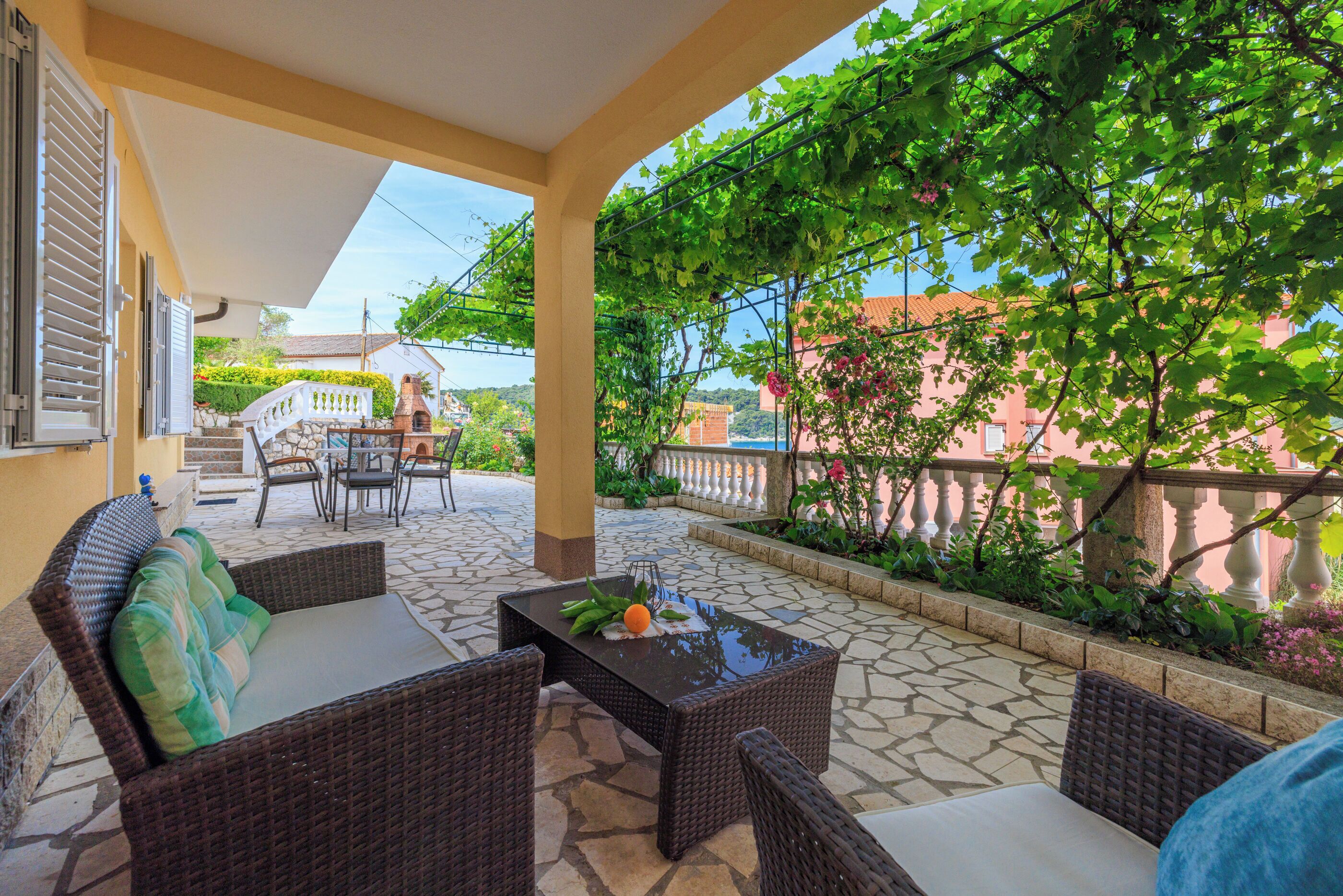 Un patio al aire libre con mobiliario de mimbre, una mesa con fruta y vistas a un edificio de fachada rosa.