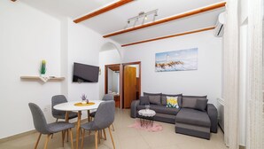 A modern living room with a dining area, a sofa, a TV, and a painting on the wall. - Apartments Ljubica (Kampor)