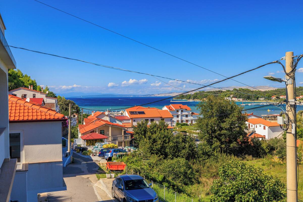A coastal village with terracotta-roofed houses, a clear blue sky, and a view of the sea.