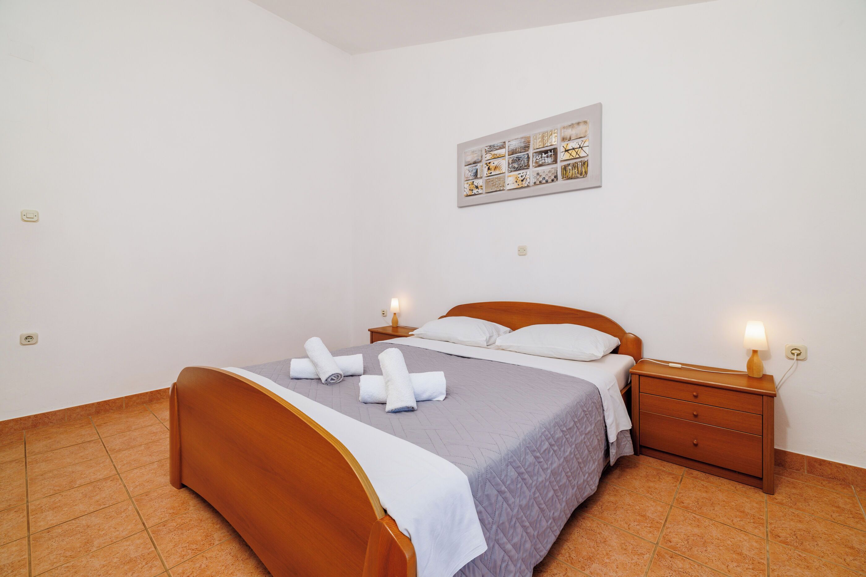A neatly made bed with a wooden headboard, a bedside table with a lamp, and a wall-mounted artwork above the bed.