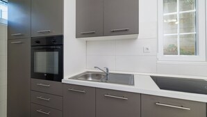 Ett modernt kök med en inbyggd ugn, en diskho i rostfritt stål och ett fönster med utsikt över grönområden.