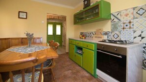 Uma cozinha com uma mesa de madeira, cadeiras, um armário verde e um fogão.