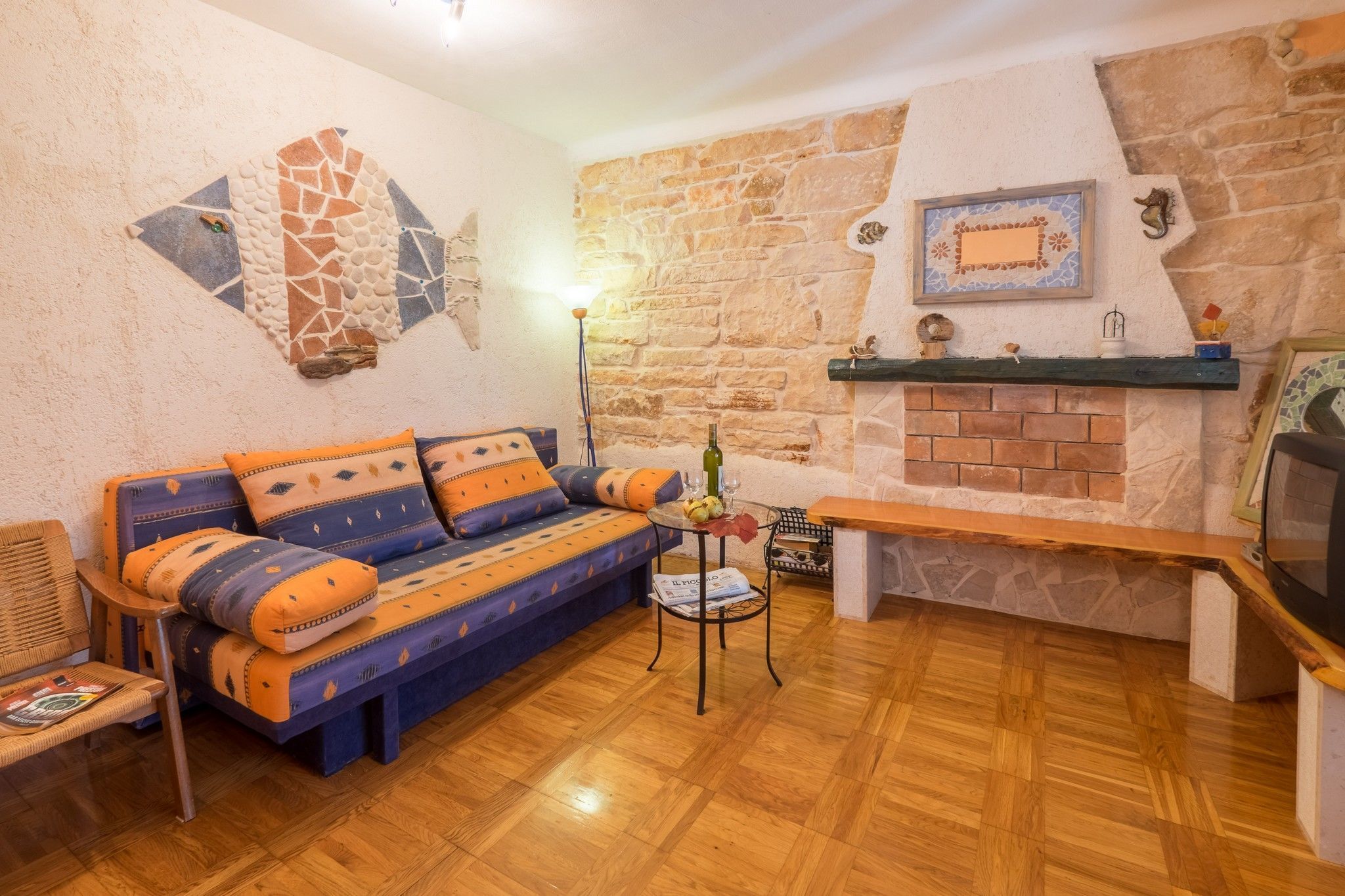 A cozy living room with a stone wall, a fireplace, a sofa with patterned cushions, and a wooden floor.