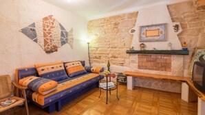 Uma sala de estar acolhedora com parede de pedra, lareira, sofá com almofadas estampadas e chão de madeira.
