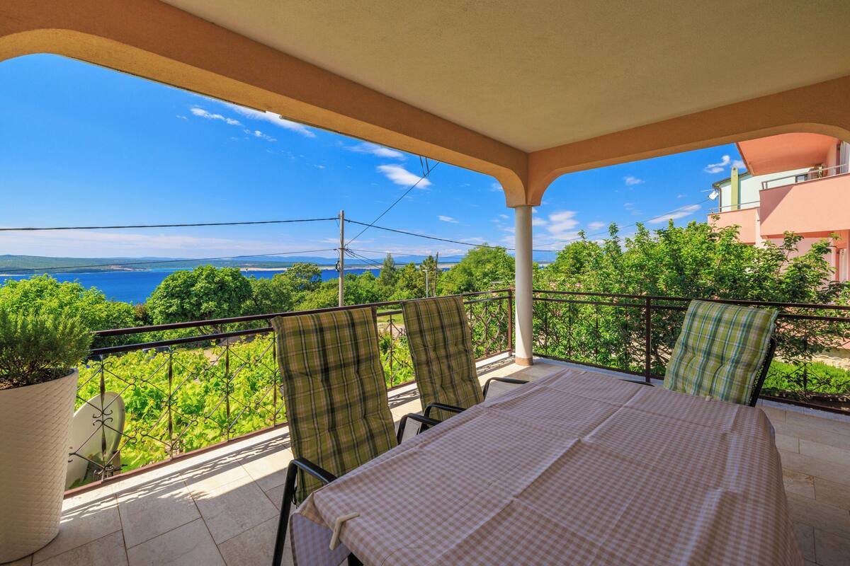 A balcony with a checkered tablecloth, two plaid chairs, and a potted plant.
